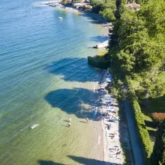 Słoneczny dzień nad jeziorem Como. Ludzie odpoczywają na plaży i pływają w krystalicznie czystej wodzie.