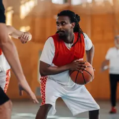 Un joueur de basket concentré, ballon en main, en plein match. Le basket fait-il grandir ? Peut-être pas en taille, mais en esprit d'équipe !