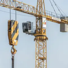 Żółty dźwig budowlany z kabiną operatora i hakiem. Widać fragmenty konstrukcji i logo Liebherr.