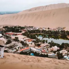Oaza na pustyni Huacachina, z turystką na wydmie pozdrawiającą zieloną, bujną okolicę z jeziorem i hotelami.