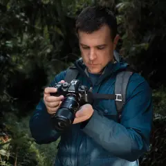 Mężczyzna w lesie trzyma aparat OM-1 Olympus, przygotowując się do makrofotografii sprzętu.