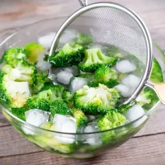 Frisch geschnittener Brokkoli wird in einer Eisschüssel abgekühlt, um das Brokkoli blanchieren zu perfektionieren. Ein Sieb hilft beim Herausnehmen.