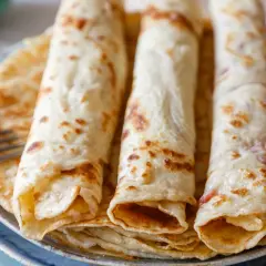 Drei goldbraune Pfannkuchen, aufgerollt und gestapelt, ein sehr gutes Pfannkuchen Rezept, bereit zum Genießen. Eine Gabel liegt daneben.