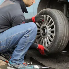 Mechanik w rękawiczkach sprawdza oponę samochodu na podnośniku.