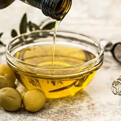 Olio d'oliva versato in una ciotola, pronto per friggere. Olive verdi e un pestello completano la scena.