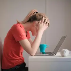 Donna con le mani tra i capelli, frustrata davanti al laptop. La cistite è rabbia repressa, un peso che schiaccia.