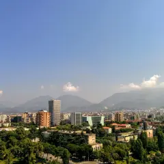 Widok na miasto z górami w tle. Widać nowoczesne budynki i zieleń. To ekuz Albania.