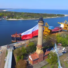 Najwyższa latarnia w Polsce z polską flagą, obok statku i portowych dźwigów.