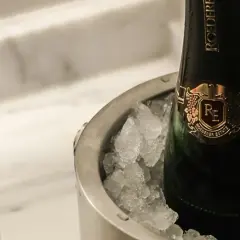 Eine Flasche Champagner in einem Eisbehälter, daneben ein Glas mit prickelndem Wein. Perfekt gekühlt, wann gefriert wein?