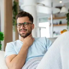 Mężczyzna z bólem gardła, okryty kocem, martwi się o utratę dochodu.
