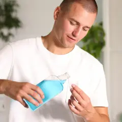 Uomo versa collutorio blu in un misurino. Curasept a cosa serve? Per un alito fresco e una bocca sana.