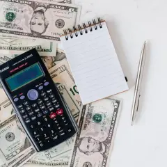 Dolarowe banknoty, kalkulator Casio, notatnik i długopis na białym tle.