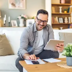 Uśmiechnięty mężczyzna z tabletem i telefonem na stoliku, szuka informacji o tym, ile wynosi podatek belki od lokat.
