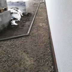 Niedokończony podjazd do domu, z paletami kostki brukowej i żwirem.