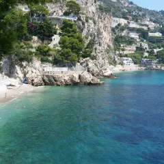Spiaggia di Eze-sur-Mer con ville aggrappate alla scogliera e acque turchesi cristalline.