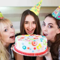 Tre amiche festeggiano con una torta colorata, pronte a soffiare le candeline per un addio al nubilato indimenticabile.