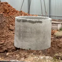 Betonowy krąg opuszczany do wykopu. Zastanawiasz się, ile kosztuje założenie szamba? To pierwszy krok do jego budowy.