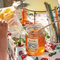 Słoik z miodem ziołowym, cytryny i kolorowe słomki na stole z wiśniami. Dziecko pije napój.