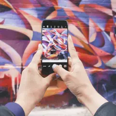 Zdjecie na Instagrama: ręce trzymają telefon, robiąc zdjęcie kolorowego muralu.