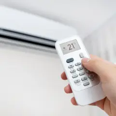 Mano ajustando el control remoto del aire acondicionado a 21°C en modo cooling. Perfecto para el heat cool en español.