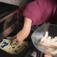 Ręka wkłada frytki do frytkownicy, przygotowując pyszne dania z airfryer przepisy po polsku.