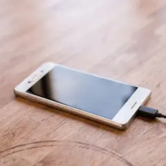 Biały smartfon podłączony do ładowarki. Zastanawiasz się, jaka jest moc ładowarki do telefonu w watach, aby szybko naładować urządzenie.