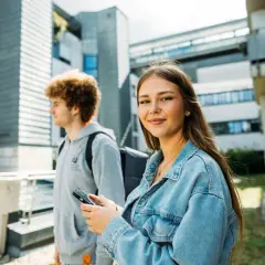 Zwei Studierende vor moderner Architektur. Sie lächelt in die Kamera, er blickt zur Seite. Ist die IU privat?
