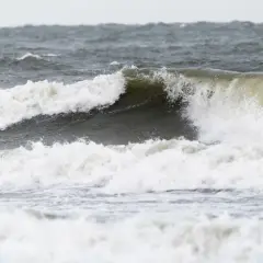 Potężne fale rozbijają się o brzeg, pokazując siłę, kiedy są sztormy na Bałtyku. Woda jest wzburzona i szara.
