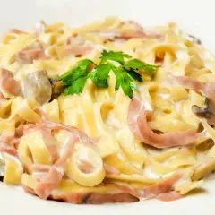 Tagliatelle z szynką i pieczarkami w kremowym sosie, z dodatkiem mozzarelli, udekorowane natką pietruszki.