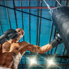 Man i boxningshandskar tränar sparra boxning mot en sandsäck i ett gym.