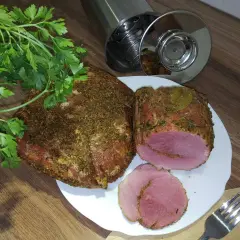 Schab w szynkowarze, przyprawiony i gotowy do krojenia. Obok świeża natka pietruszki i widelec.