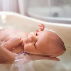 Malutkie dzieci w kąpieli, delikatnie unoszone na wodzie. Rączka rodzica podtrzymuje główkę niemowlaka, tworząc bezpieczną przestrzeń do relaksu.