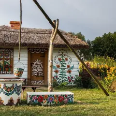 Kolorowy dom z malowanymi kwiatami, studnia i ławka. Zalipie atrakcje zachwycają ludowym pięknem.