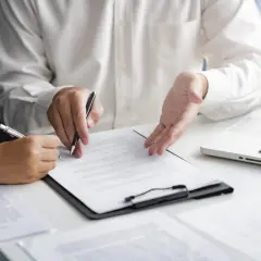 Deux personnes discutent d'un document, l'une signant, l'autre expliquant. Une commission d'intervention est en cours.