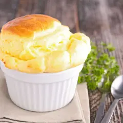 Un délicieux soufflé au fromage, doré et gonflé, servi dans un ramequin blanc sur une table en bois rustique.