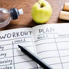 Plan na **full body workout** w zeszycie, obok jabłka, butelki wody i hantli.