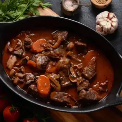 Un riche bœuf bourguignon mijoté, avec des morceaux de viande tendres, des carottes et des champignons, prêt à être dégusté avec un verre de pinot noir.