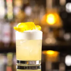 Klasyczny whisky sour przepis: orzeźwiający koktajl z pianką i skórką cytryny na tle rozmytego baru.