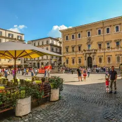 Piazza animata con persone che passeggiano e si godono un caffè all'aperto, un assaggio delle serate Erasmus a Roma.