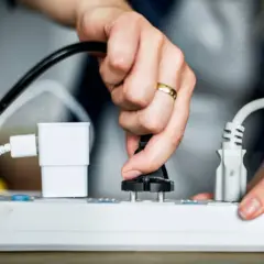 Ręka wyciąga wtyczkę z listwy zasilającej, by obniżyć rachunki za prąd PGE. Oszczędzaj energię!