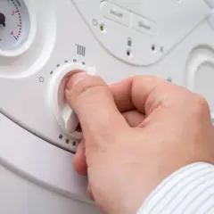 Mano che regola la temperatura caldaia termosifoni. Quadrante bianco con simboli di riscaldamento e manopola.