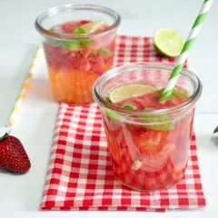Orzeźwiający drink z truskawkami, miętą i limonką, podany w szklance z zielono-białą słomką. Obok leży świeża truskawka.