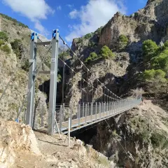 Puente colgante en la ruta del saltillo, con imponentes montañas rocosas y vegetación verde.