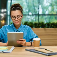 Studentka w okularach korzysta z iPada na studia, siedząc przy biurku z kawą i notatkami.