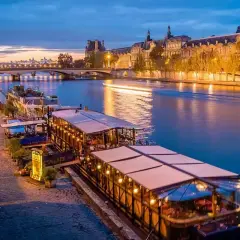 Un restaurant sur Seine à Paris, illuminé et accueillant, reflète ses lumières sur l'eau paisible.