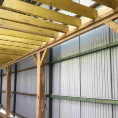 Structure en bois avec madriers ou bastaings soutenant un toit, le long d'un mur en tôle ondulée.