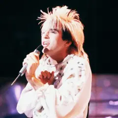 Limahl piosenkarz z charakterystyczną fryzurą śpiewa do mikrofonu na scenie.