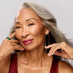 Mujer con canas, anillos y pendientes llamativos. Su cabello plateado ondea suavemente, como si tuviera 30 años de sabiduría y estilo.