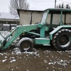 Zielona ładowarka Ostrówek KTO-162 stoi na błotnistym podwórku, pokryta śniegiem.