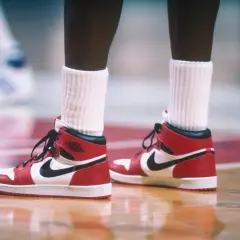 Rote und weiße Air Jordan 1 Sneaker mit schwarzem Nike-Logo auf einem Basketballplatz. Ein ikonisches Stück der Geschichte des Nike-Unternehmens.